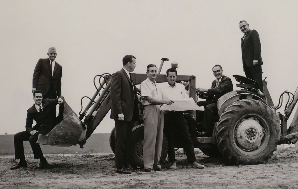 Black and white photo of Ray Watt, founder of Watt Companies, sitting on a tractor with associates
